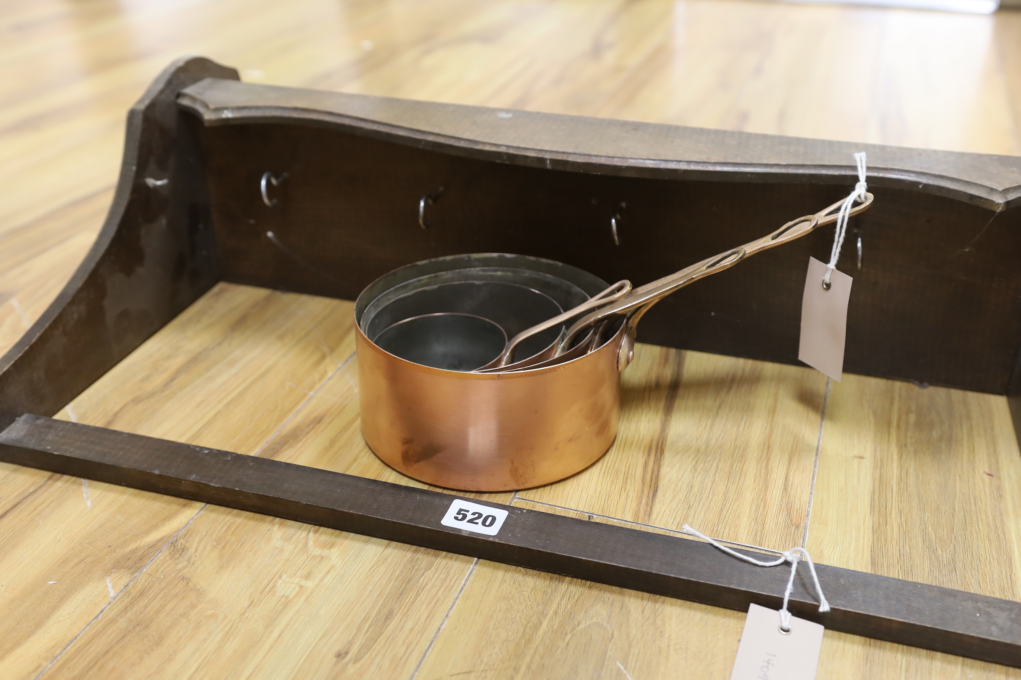 A graduated set of four copper and brass handled saucepans with a beech hanging wall rack, rack approximately 64cm wide